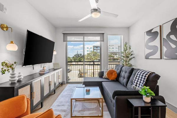 Modern apartment living room with gray sectional sofa, wall-mounted TV, and balcony overlooking city buildings